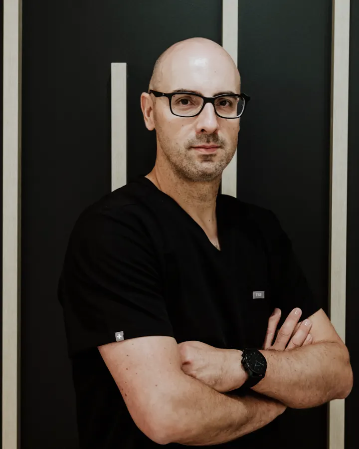 El Dr. Daniel Quirós, con pijama clínico negro y los brazos cruzados, en su consulta.